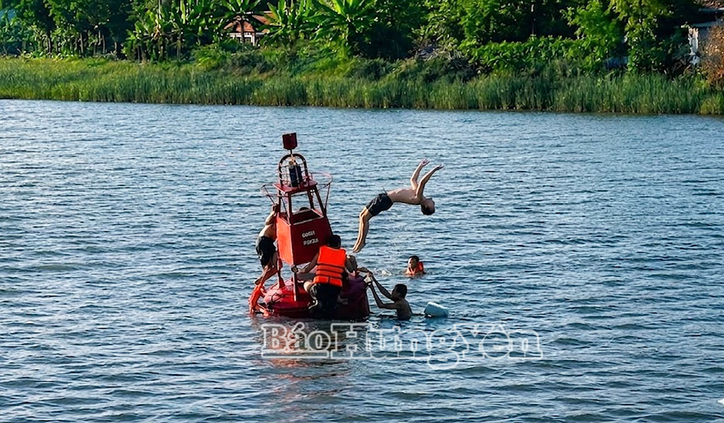 Nhiều thanh thiếu niên bám lên ụ nổi giữa sông để nhảy xuống nước, hành vi tiềm ẩn rủi ro đuối nước.