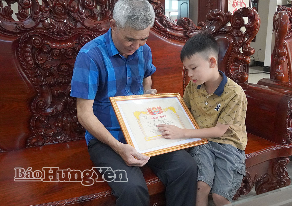 Cựu chiến binh Mai Thanh Thuần kể lại chiến công tiêu diệt giặc Mỹ được tặng bằng khen cho cháu nội nghe.